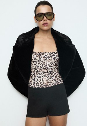 Un manteau en fausse fourrure noire, un body à imprimé léopard et un short noir. De grandes lunettes de soleil teintées complètent le look.