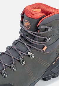 Botte de trekking noire et grise avec un col en maille rouge rembourré, des crochets en métal et une semelle en caoutchouc renforcée. Présente un logo d'éléphant.