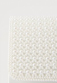 Λευκός υφασμάτινος κουτί διακοσμημένο με συστάδες από λευκές, γυαλιστερές πέρλες διαφορετικού μεγέθους που καλύπτουν την πάνω επιφάνεια, δημιουργώντας τρισδιάστατο εφέ.