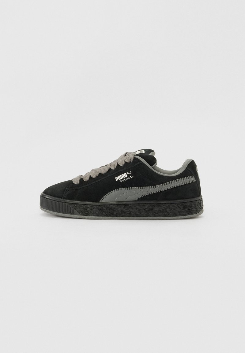 Black suede sneakers with a textured rubber sole, gray accents, and thick laces. Features a prominent logo on the side and rear.