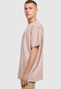 Camiseta de algodón de color rosa claro con un corte relajado, mangas cortas, escote redondo y detalles de costura mínimos, llevada por un modelo masculino.