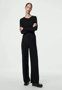 Top preto de manga longa combinado com calças pretas plissadas de cintura alta. Textura suave e design de perna reta, completado com sapatos pretos planos.