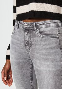 Jeans ajustados gris con un ligero desvanecimiento, diseño de cinco bolsillos, cierre con botón de metal y detalles de costura sutiles, combinados con una blusa a rayas en blanco y negro.