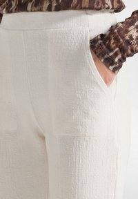 Witte textuur broek met een relaxed fit, voorzien van zijzakken en een subtiel patroon. De stof lijkt lichtgewicht en ademend.
