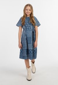 Blå mönstrad klänning med korta ärmar, åtsittande midja och utsvängd kjol, i kombination med beige ankelstövlar.