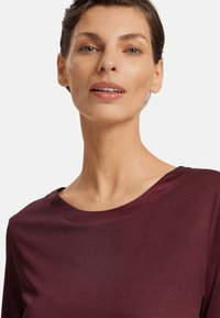 Burgundy topp med en slät, mjuk textur, bred rund halsringning och trekvartsärmar, som framhäver en enkel, modern design.