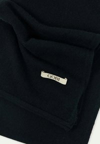 Svart cashmere-scarf med mjuk textur, prydd med en GOBI-etikett i silver på en vikta kant. Enkel och elegant design.