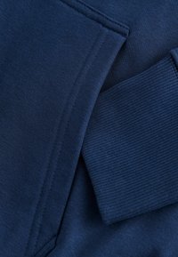 Tissu de sweat-shirt bleu marine avec une texture lisse, doté d'un poignet côtelé. La couture est propre et finie de manière uniforme.