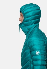 Teal pufferjakke med hætte, der viser kviltet tekstur og snøre lukning. Har et logo på venstre skulder.