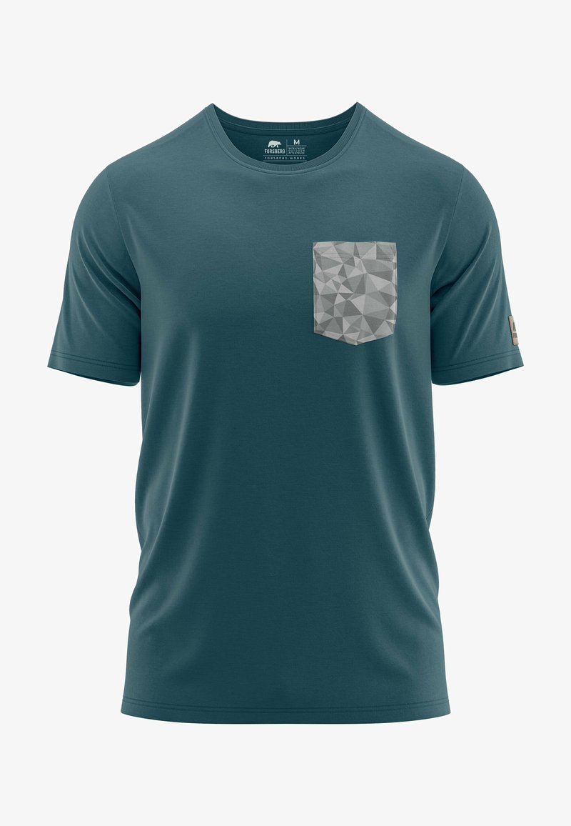 Camiseta de manga corta color teal, hecha de una tela suave, presenta un bolsillo en patrón geométrico gris en el lado izquierdo del pecho. Cuello redondo con una etiqueta.