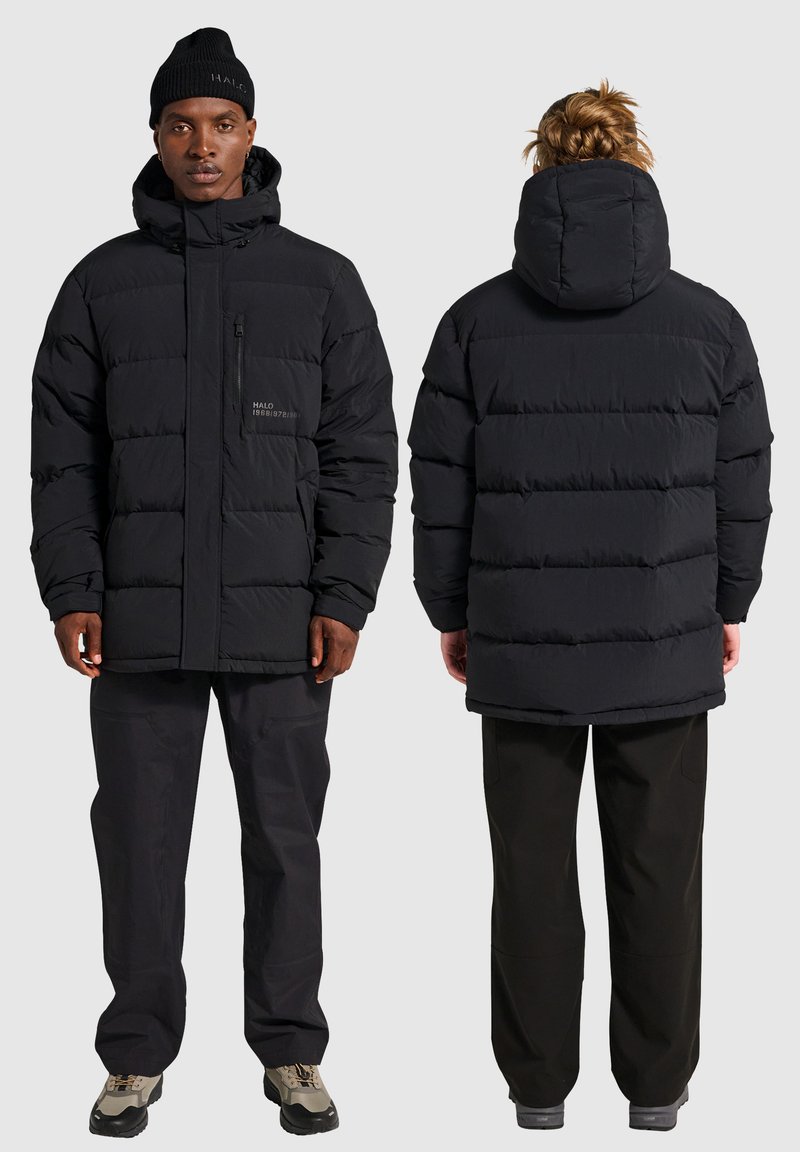 Sort pufferjakke med lynlås foran, hætte og logo-detalje. Har tykke, quiltede paneler og en afslappet pasform. Bæres med matchende mørke bukser.