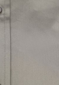 Lichtgrijze stof met een gladde textuur, voorzien van een diagonale weefpatroon. Inclusief een verticale naad en een ronde, donkere knoop.