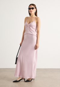 Abito senza maniche in satin rosa con corpetto aderente e gonna fluida. Abbinato a scarpe con tacco nere a punta e una piccola borsa nera.