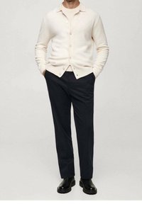 Light beige cardigan, textured knit, buttoned front; paired with dark trousers and black, chunky-soled boots; minimalistic design.