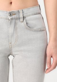 Jean en denim gris clair à taille haute, avec des coutures discrètes et des poches standard. Le tissu a une texture lisse et une coupe classique.