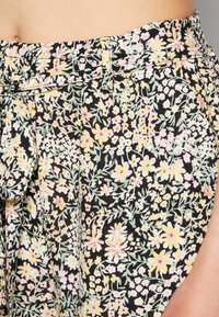 Tejido negro con un estampado floral en amarillo, rosa y verde. Presenta una cinturilla ancha y una abertura lateral para un ajuste relajado.