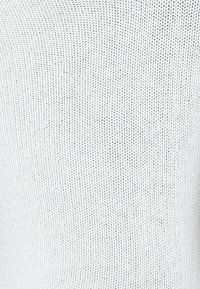 Tissu en tricot blanc avec un motif fin et texturé. Le design présente de petites ouvertures régulières, créant une apparence légère.