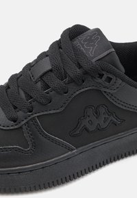 Fekete sneaker szintetikus anyagból, kerek fűzőkkel, varrott részletekkel és texturált talppal. Kappa logó dombornyomott oldalán.