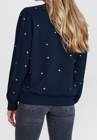 Marinblå sweatshirt med en mjuk textur, prydd med spridda metalliska diamantaccenter och en ribbad nederdel. Ärmarna har en puffad design.