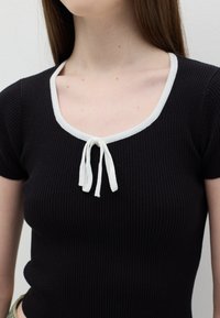 Top nero a maniche corte con costine, caratterizzato da un collo a contrasto bianco e un dettaglio di annodatura frontale. Design aderente con tessuto testurizzato.
