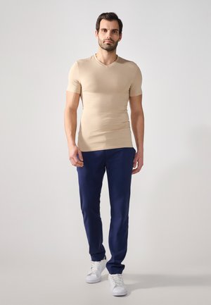Beige lyhythihainen V-pääntie t-paita, yhdistettynä tummansinisiin housuihin ja valkoisiin lenkkareihin. Sileä pinta, istuva muotoilu ja minimalistinen tyyli.