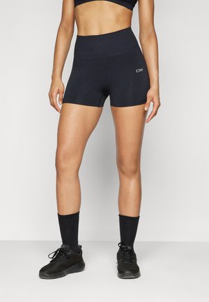 Shorts de sport noirs avec une taille haute, texture lisse et un petit logo sur le côté. Associés à des chaussettes noires et des baskets.