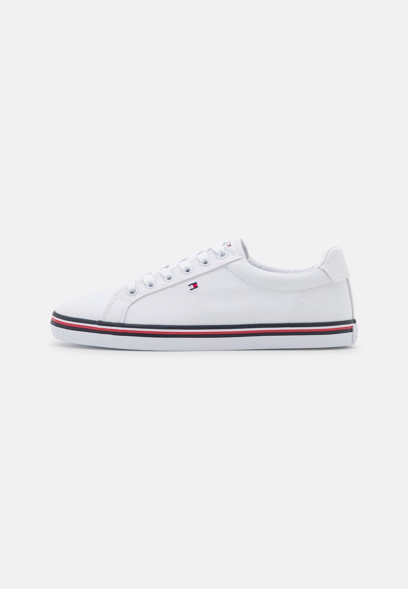 Sneaker bianco in tela con punta tonda, chiusura con lacci sul davanti e lati testurizzati. Presenta una striscia rossa e blu sulla suola e un logo sul lato.