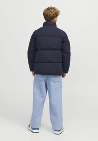 Marineblaue Steppjacke mit hohem Kragen, mit gesteppten Abschnitten und schmaler Passform. Kombiniert mit lockeren hellblauen Jeans und Sneakers.