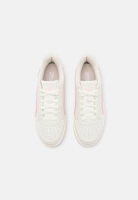 Paire de baskets blanches Puma avec des accents roses, lacées, vues de dessus sur un fond gris clair uni.