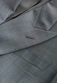 Gros plan d'une veste de costume à carreaux gris montrant le revers, la boutonnière et la poche poitrine avec un tissu finement texturé.