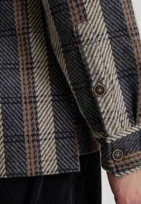 Wool jakna s uzorkom houndstooth u mornarsko plavoj, krem i hrđavoj boji, s dugmadi na manžetama i teksturiranim završetkom.