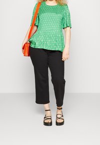 Grøn peplum-top med hvide blomsterdetaljer, korte ærmer, parret med sorte cropped bukser og sorte sandaler med remme. Orange crossbody taske.