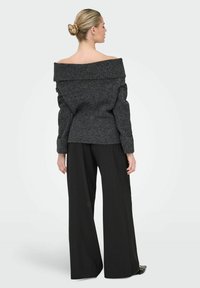 Sweter w kolorze ciemnoszarym, dzianinowy, z opadającymi rękawami i szerokimi rękawami, o teksturowanej tkaninie, połączony z czarnymi spodniami o wysokim stanie i szerokich nogawkach.