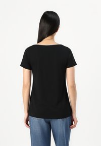 Black short-sleeve t-shirt with a round neckline and a soft texture; viewed from the back. Paired with medium-wash blue denim jeans.