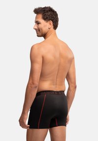 Schwarze Boxershorts mit roten Akzenten, mit einem elastischen Bund, der mit "DANISH" beschriftet ist, und einem körperbetonten Schnitt. Glatte Stofftextur.
