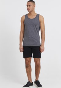 Gray cotton tank top with a round neckline, paired with black shorts. The model wears black sneakers and has a visible tattoo on the leg.