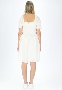 Witte jurk met een gerimpelde bodice en korte pofmouwen, met een vierkante rug en een geplooide rok. Draagt het met witte sneakers.