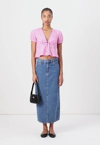 Rosa bomulls crop topp med pufferm og knytedetalj, parret med et blått denim maxiskjørt. Tilbehør inkluderer en svart håndveske og flate sko.
