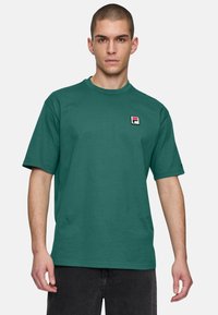 Maglietta di cotone verde con scollatura rotonda, maniche corte e un piccolo logo ricamato in un quadrato sul lato sinistro del petto. Design semplice.