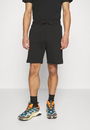 Shorts noirs en tissu doux avec une taille élastique et un cordon de serrage. Portés avec des baskets colorées dotées de détails en mesh et en synthétique.
