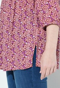 Blomsterbluse i bordeaux med pink og lilla blomster mønstre, korte ærmer og sideskåringer. Sammen med mørke denim jeans.