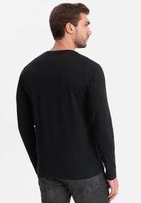 Maglietta nera a maniche lunghe in cotone, con collo tondo, design aderente e texture liscia, vista da dietro.