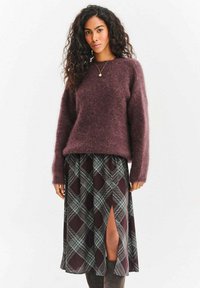 Fioletowy sweter z miękkiego materiału zestawiony z plisowaną spódnicą w kratę, z przednim rozcięciem, zielono-białe wzory na ciemnym tle. Kozaki do kolan.