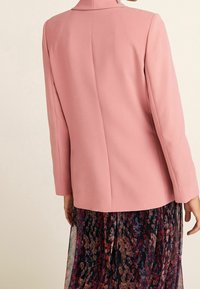 Blazer rosa con un corte estructurado, con un pequeño cuello y mangas largas, combinado con una falda de patrón floral multicolor.