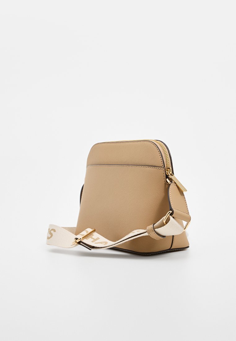 Sac à bandoulière synthétique beige avec fermeture éclair, forme arrondie, bord noir et sangle en toile avec texte beige.