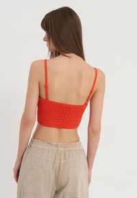 Rød kortermet strikket topp med et blomstermønster og justerbare stropper. Kombinert med beige baggy-bukser med sidelommer og en kjedeaccent.