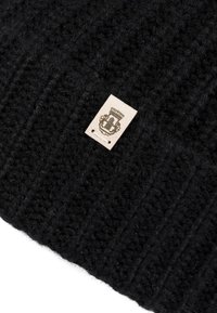 Black knitted fabric with a small beige label displaying a detailed emblem or crest stitched onto it.