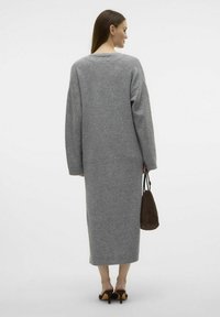 Vestido gris de manga larga y largo hasta el tobillo, hecho de tejido de punto suave, con un corte holgado y puños acanalados, combinado con un bolso marrón.