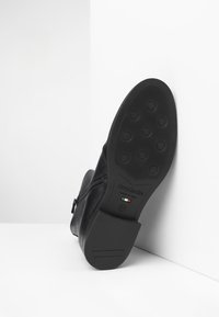 Stivaletto in pelle nera con suola in gomma testurizzata dotata di grip circolari, zip laterale e dettagli di branding che indicano la fabbricazione italiana.