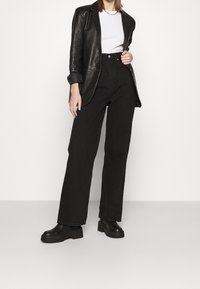 Blazer de cuero negro, camiseta blanca, pantalones de tiro alto negros y botas de plataforma. Diseño simple con una textura suave y un corte recto.